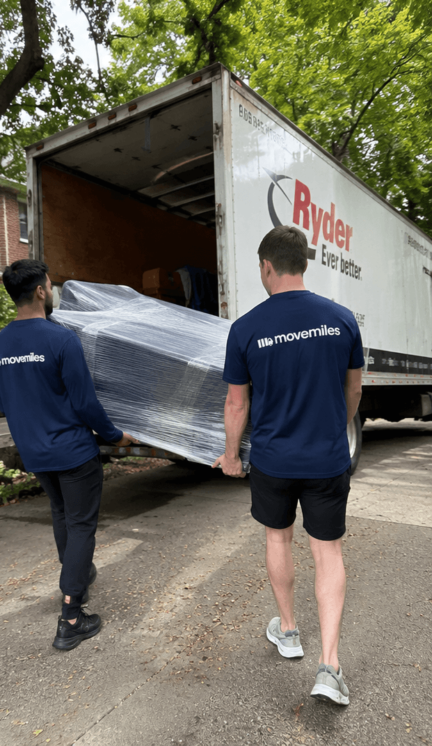Two uniformed Movemiles movers walking a wrapped item to the truck