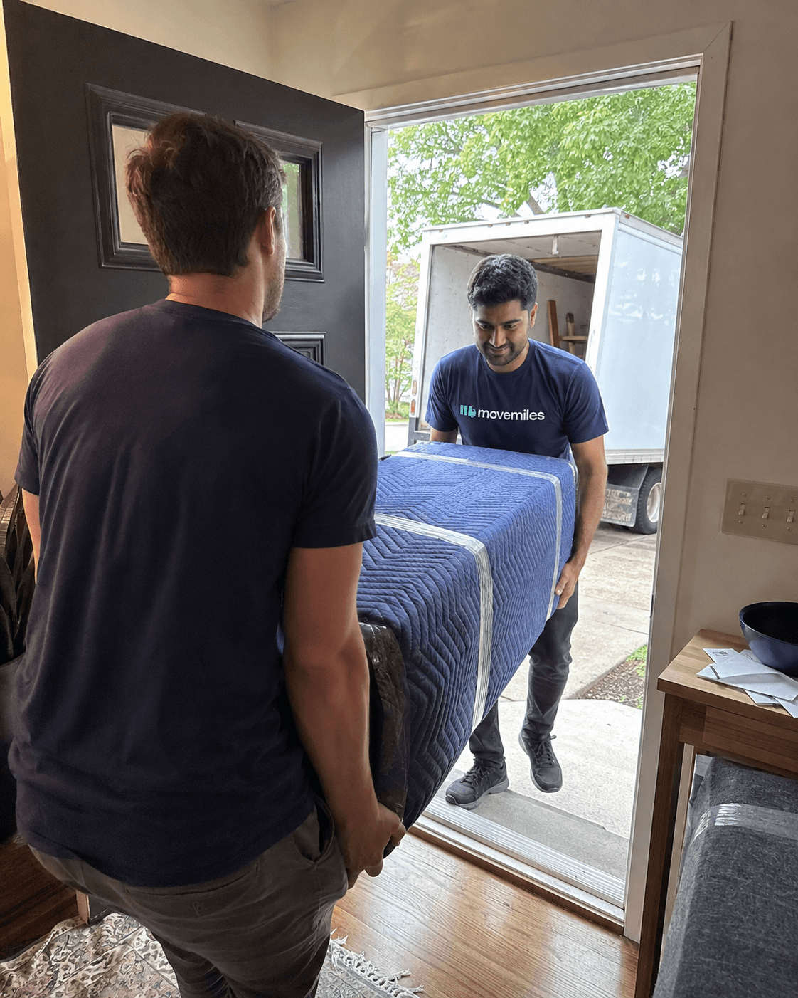 Movemiles mover bringing a wrapped item through the front door